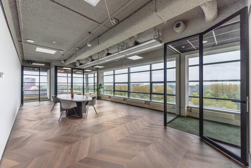 Modern meeting room with large windows, herringbone wooden floor, and city views at Joop Geesinkweg.